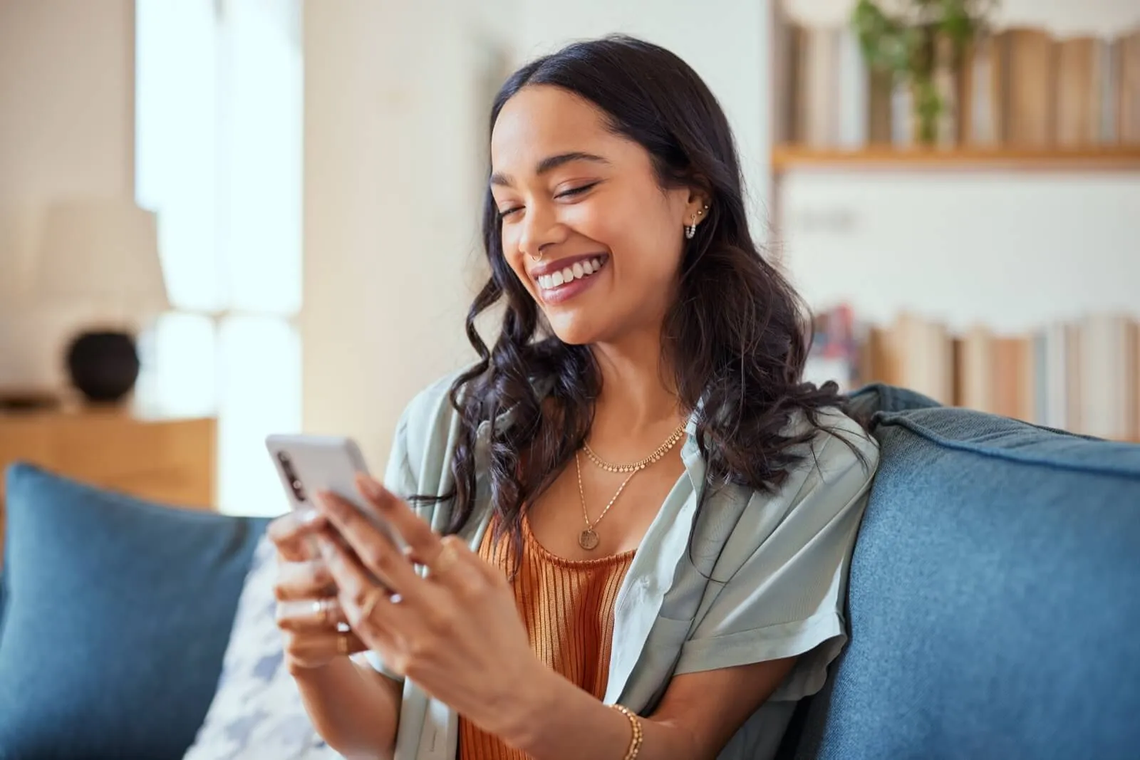 Side view of person smiling while using smartphone on blue couch in living room