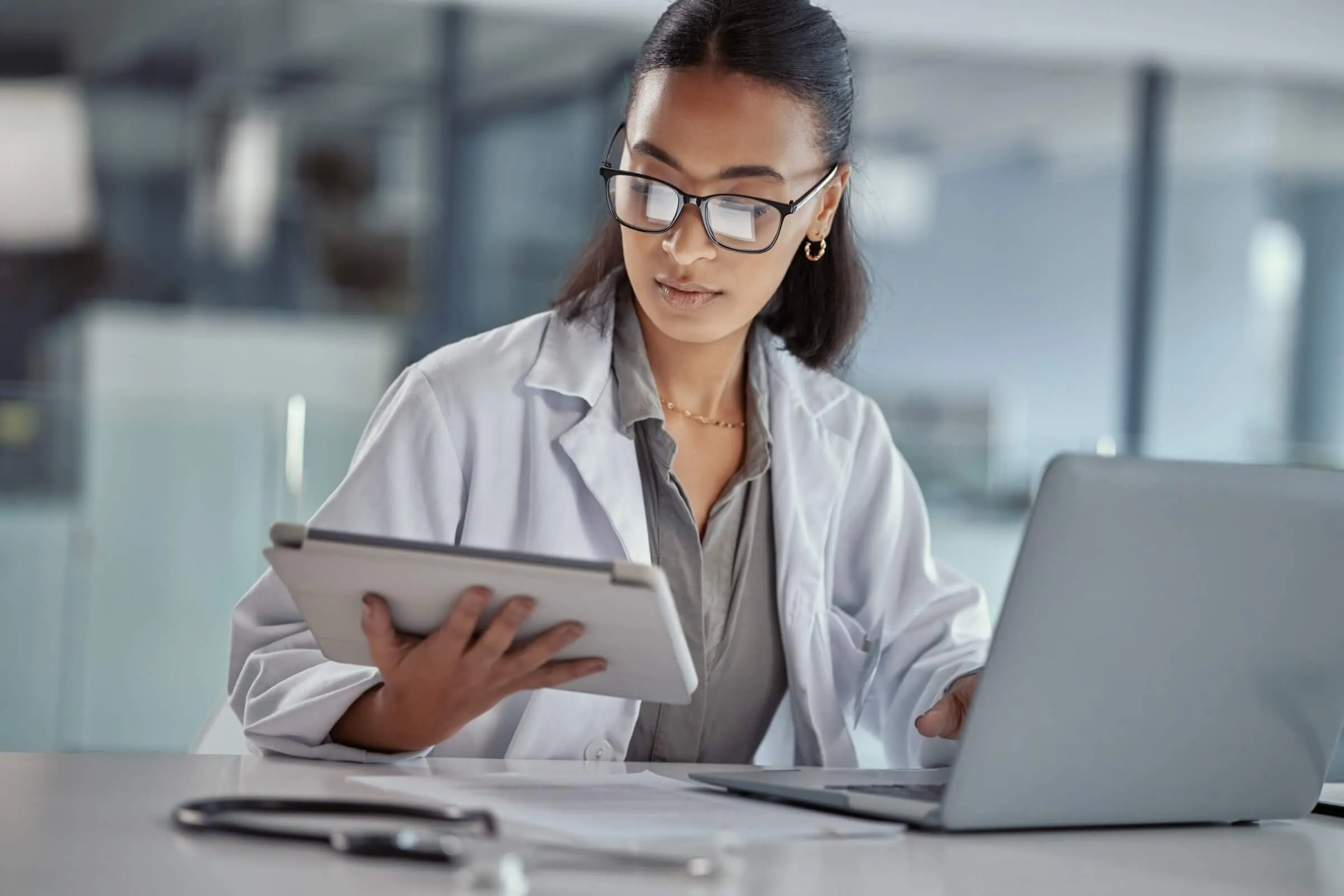 Medical researcher reviewing data between laptop and tablet in clinical environment.